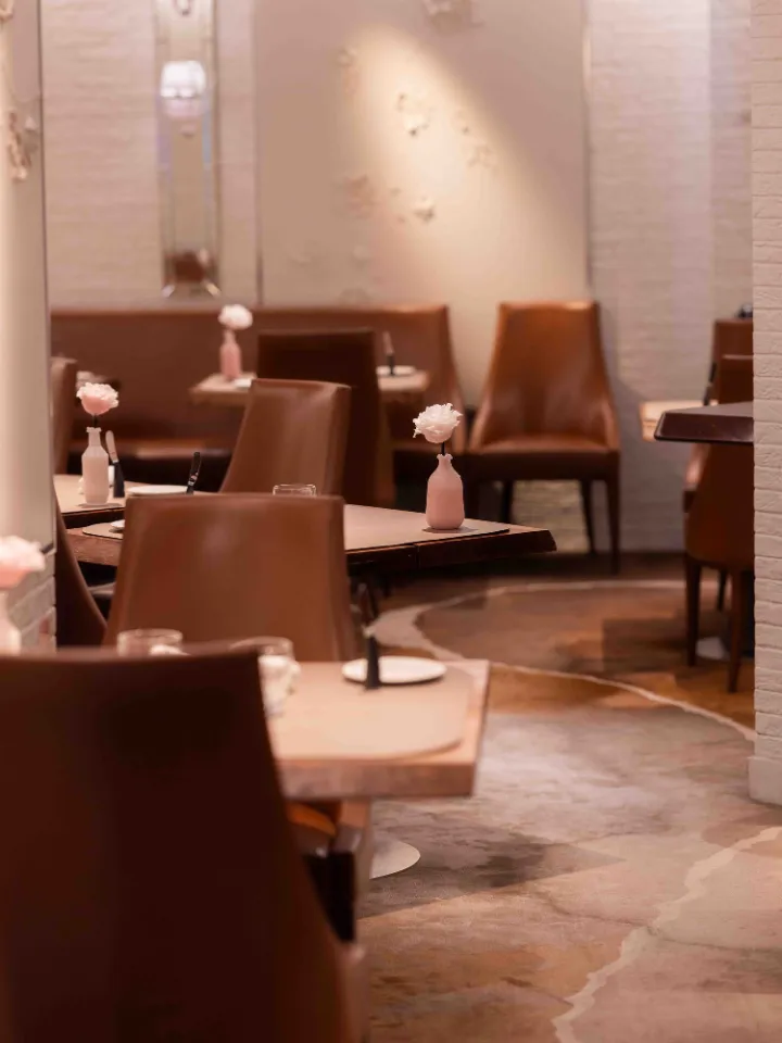 Salle à manger élégante avec des chaises en cuir marron, des tables en bois clair et des petites décorations florales roses.