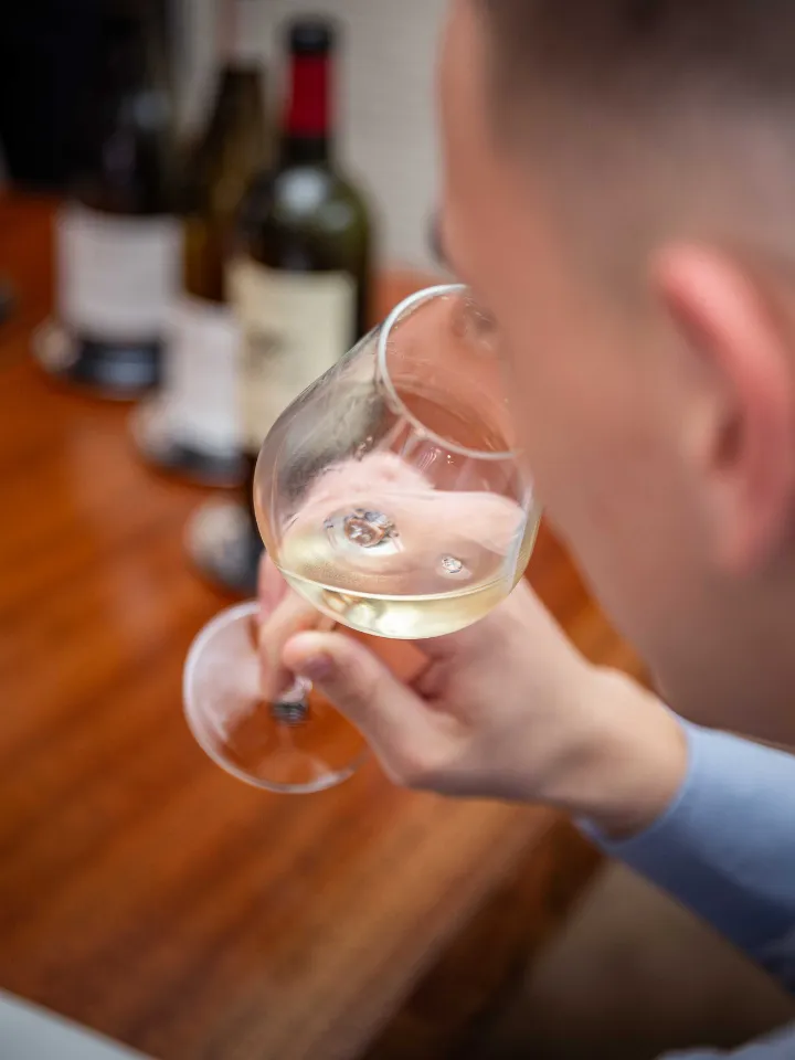 Personne tenant un verre de vin blanc avec des bouteilles floues en arrière-plan sur une surface en bois.