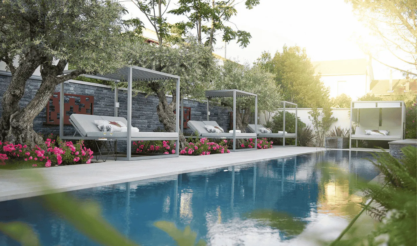 Piscine extérieure bordée de lits de repos modernes sous des pergolas, entourée d'arbres et de fleurs roses.