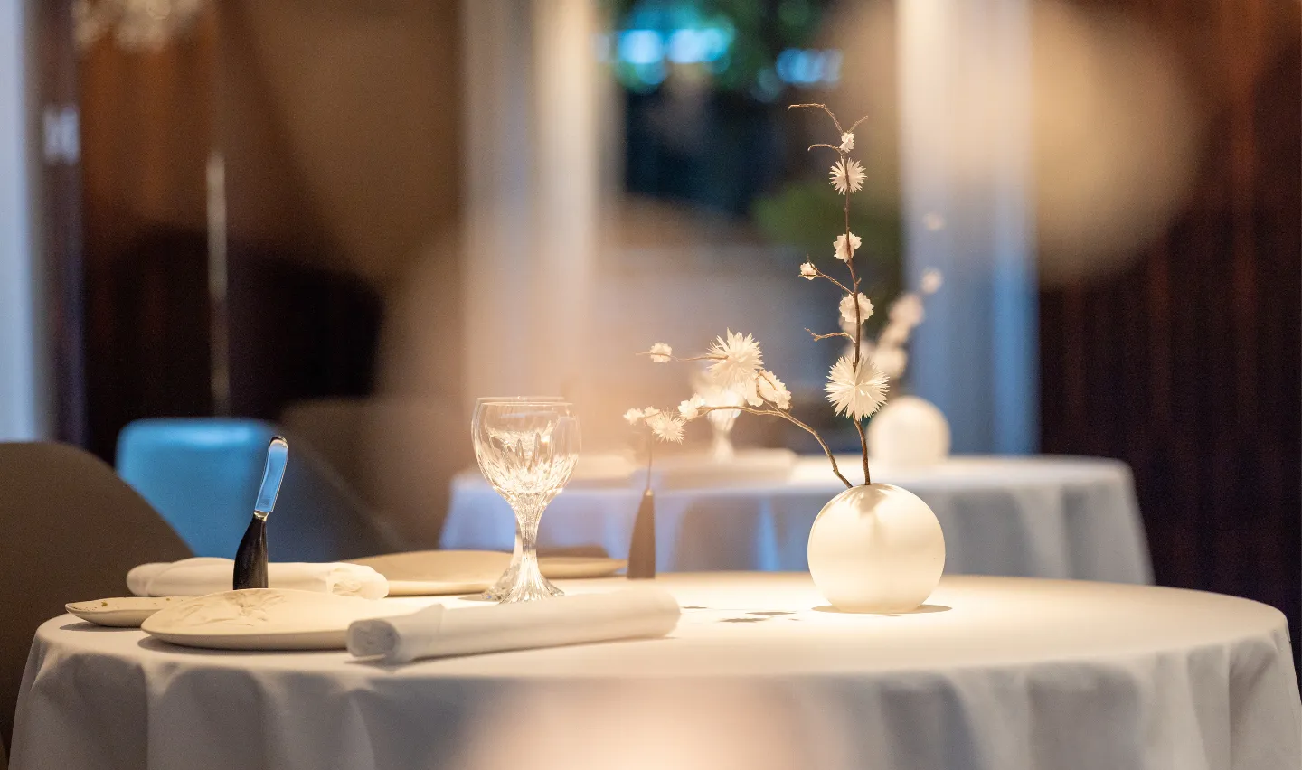 Table dressée au Restaurant Pic à Valence, avec nappe blanche, verre à vin, serviette roulée, couteau et vase de fleurs blanches délicates.
