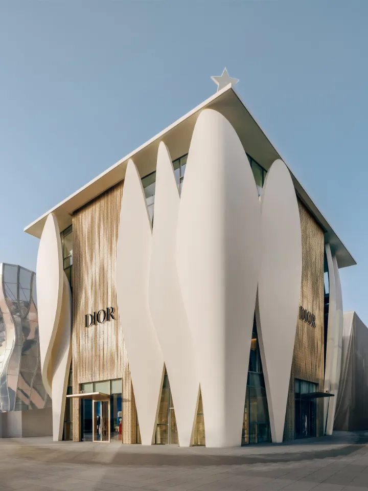 Façade moderne d'un magasin Dior avec des grandes formes blanches incurvées et une étoile au sommet du toit sous un ciel bleu.