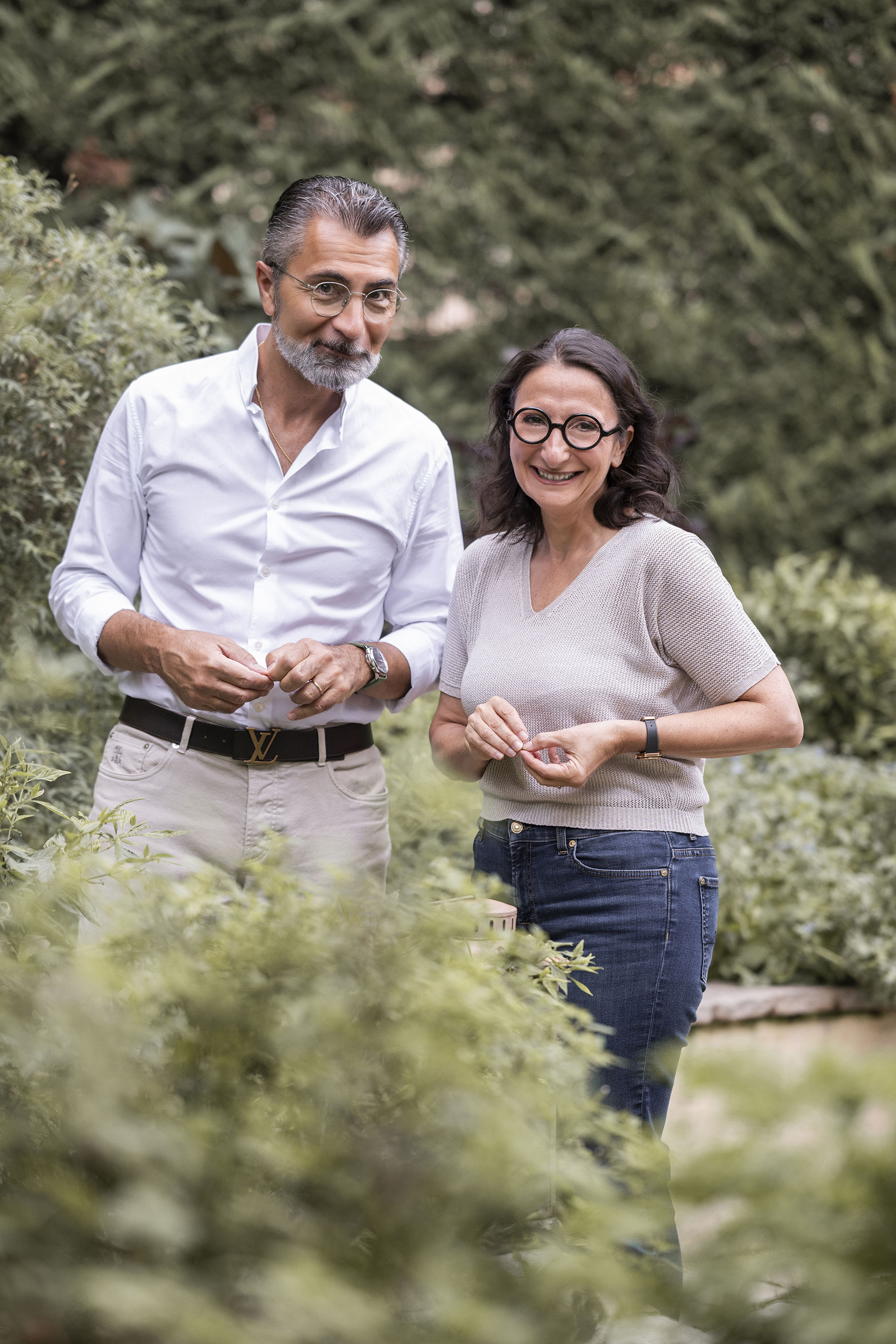 Un homme et une femme souriants debout dans un jardin verdoyant.