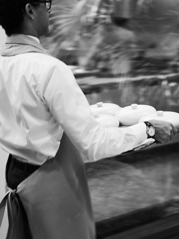 Commis de rang portant un plateau avec des assiettes couvertes en salle.