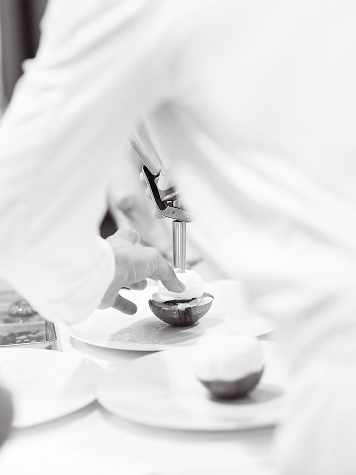 Chef de partie dressant un dessert à l’aide d’un siphon de crème en cuisine.