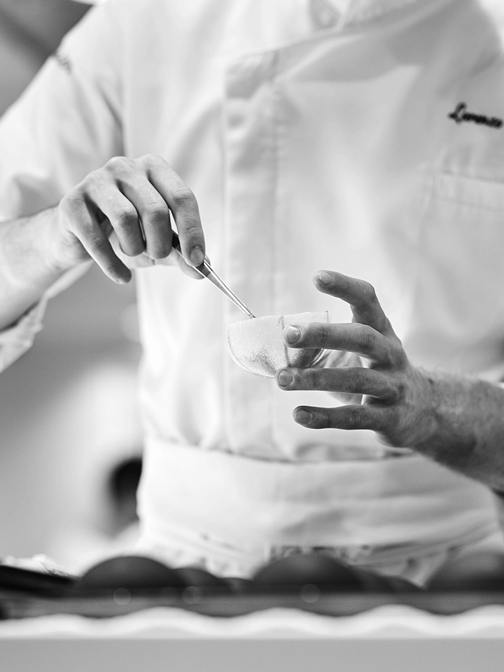 Commis de cuisine manipulant délicatement une demi-sphère à l’aide d’une pince en cuisine.