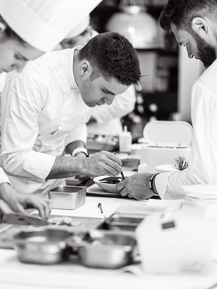 Trois chefs pâtissiers concentrés travaillant ensemble à décorer un plat dans une cuisine professionnelle.