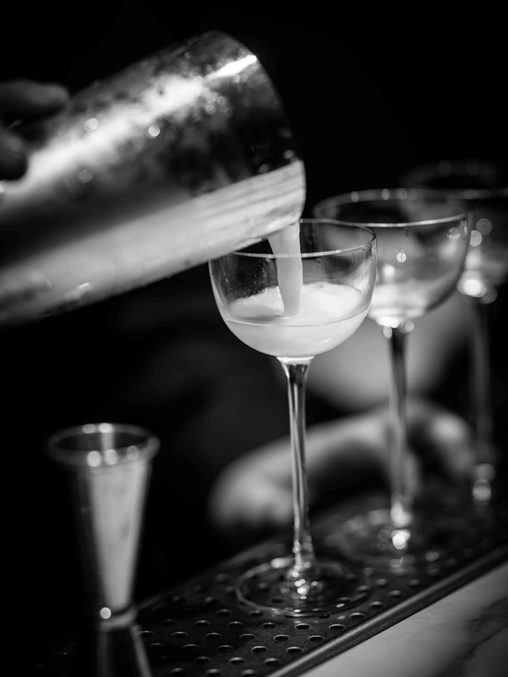 Bartender versant un cocktail d’un shaker en métal dans un verre au comptoir du bar.