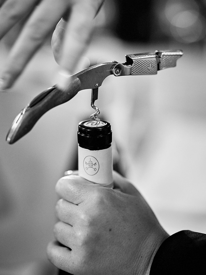 Main d’un commis sommelier ouvrant une bouteille de vin avec un tire-bouchon à levier en salle.