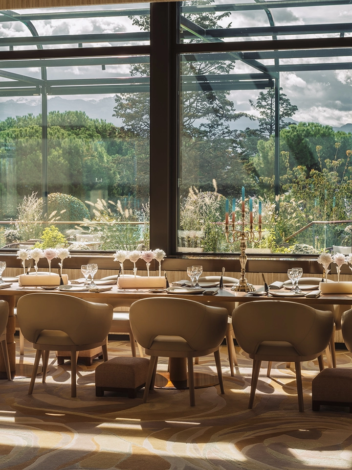 Elegant gedeckter Tisch mit Weingläsern, Servietten und Kerzenständer mit mehreren Kerzen, vor einem großen Fenster, das in einen grünen Garten führt.