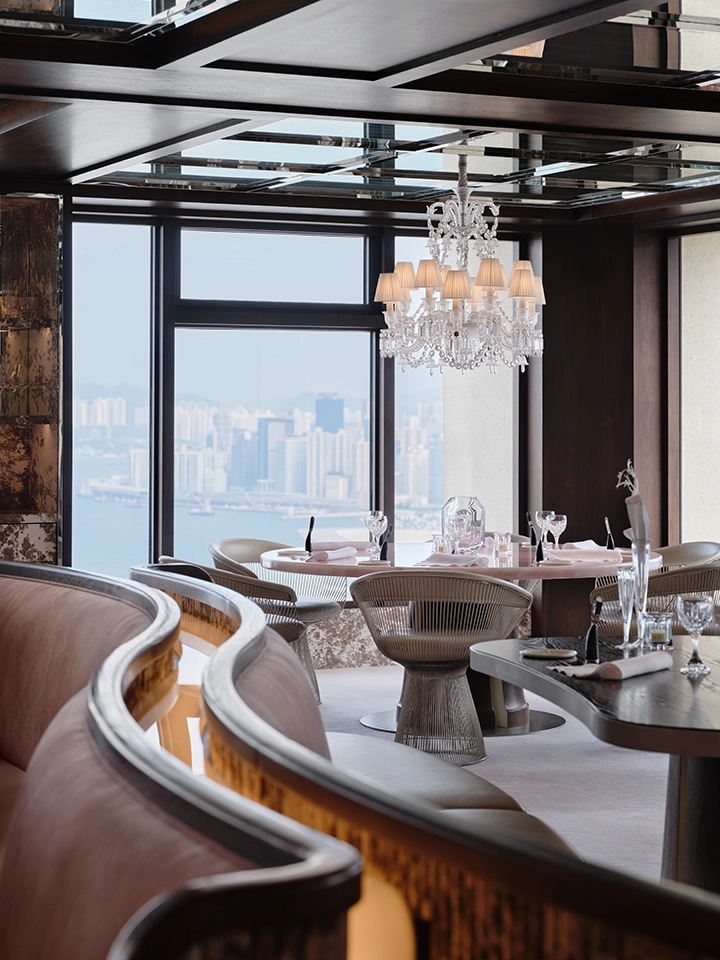 Intérieur élégant de restaurant avec banquettes incurvées, table ronde dressée, lustre en cristal et vue sur la ville à travers de grandes fenêtres.