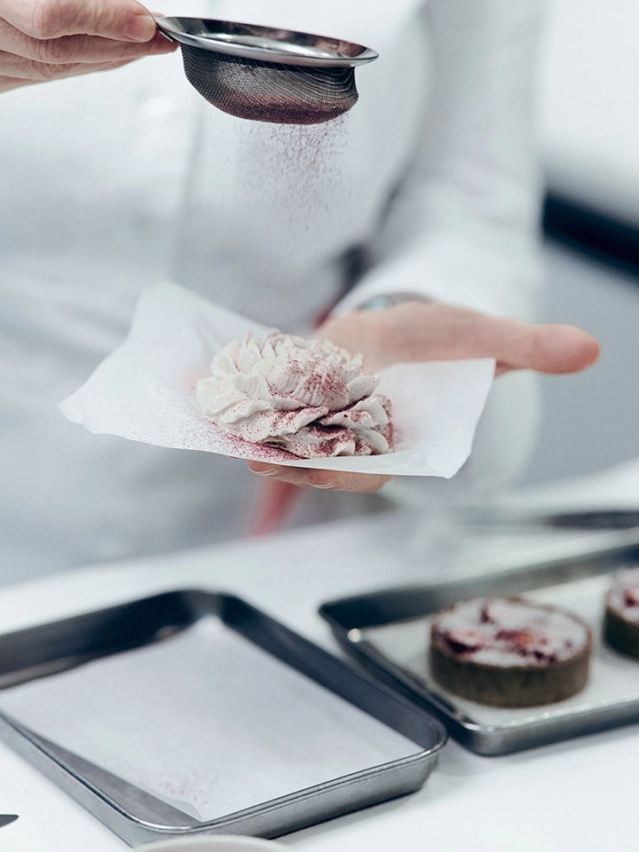 Main saupoudrant de la poudre sur une fleur de crème posée sur une feuille de papier.