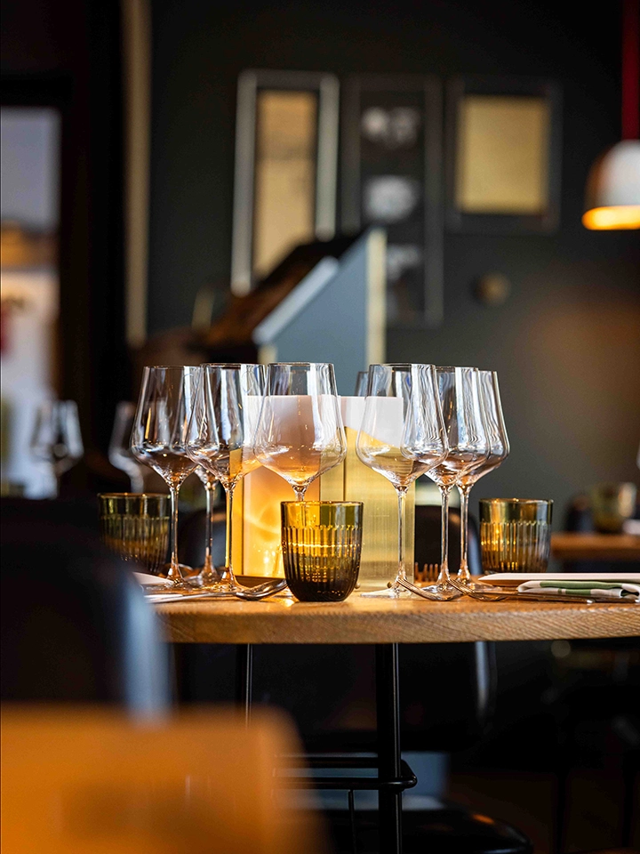 Elegant gedeckter Tisch mit mehreren Weingläsern und angezündeten Kerzen in einem Restaurant mit sanftem Licht.