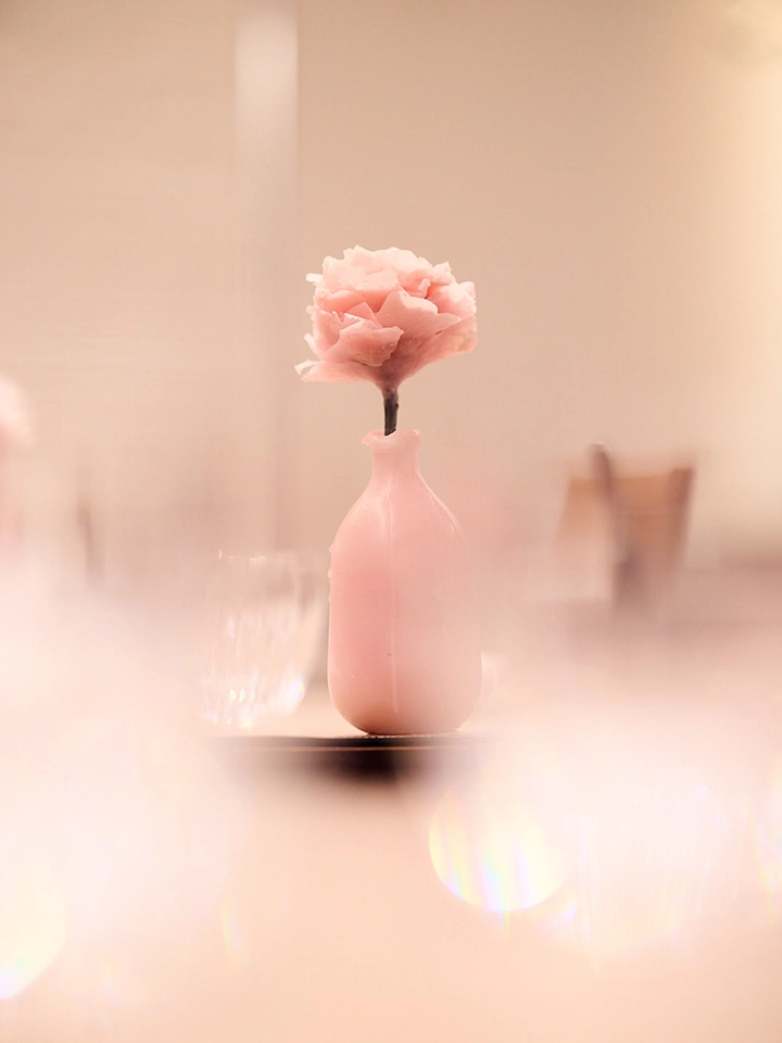 Une fleur rose délicate dans un petit vase rose sur une table floue.