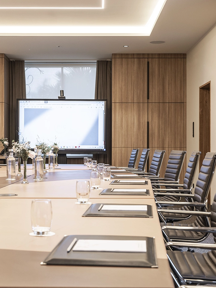 Salle de réunion moderne avec une grande table équipée de dossiers, stylos et verres, et un écran de projection sur fond de murs en bois.