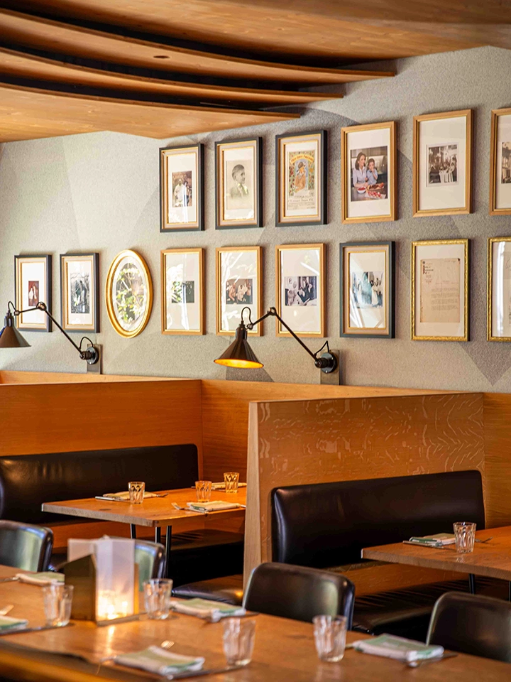 Intérieur de restaurant avec banquettes en cuir, tables en bois dressées, lampes murales et murs décorés de cadres photo.