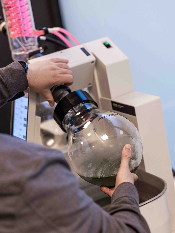 Une personne manipule un ballon en verre connecté à un appareil de laboratoire blanc.