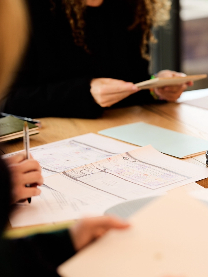 Des personnes travaillant ensemble sur des plans et des documents étalés sur une table en bois.