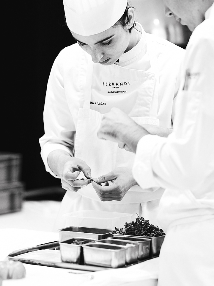 Commis de cuisine participant à la préparation des plats en restaurant gastronomique.