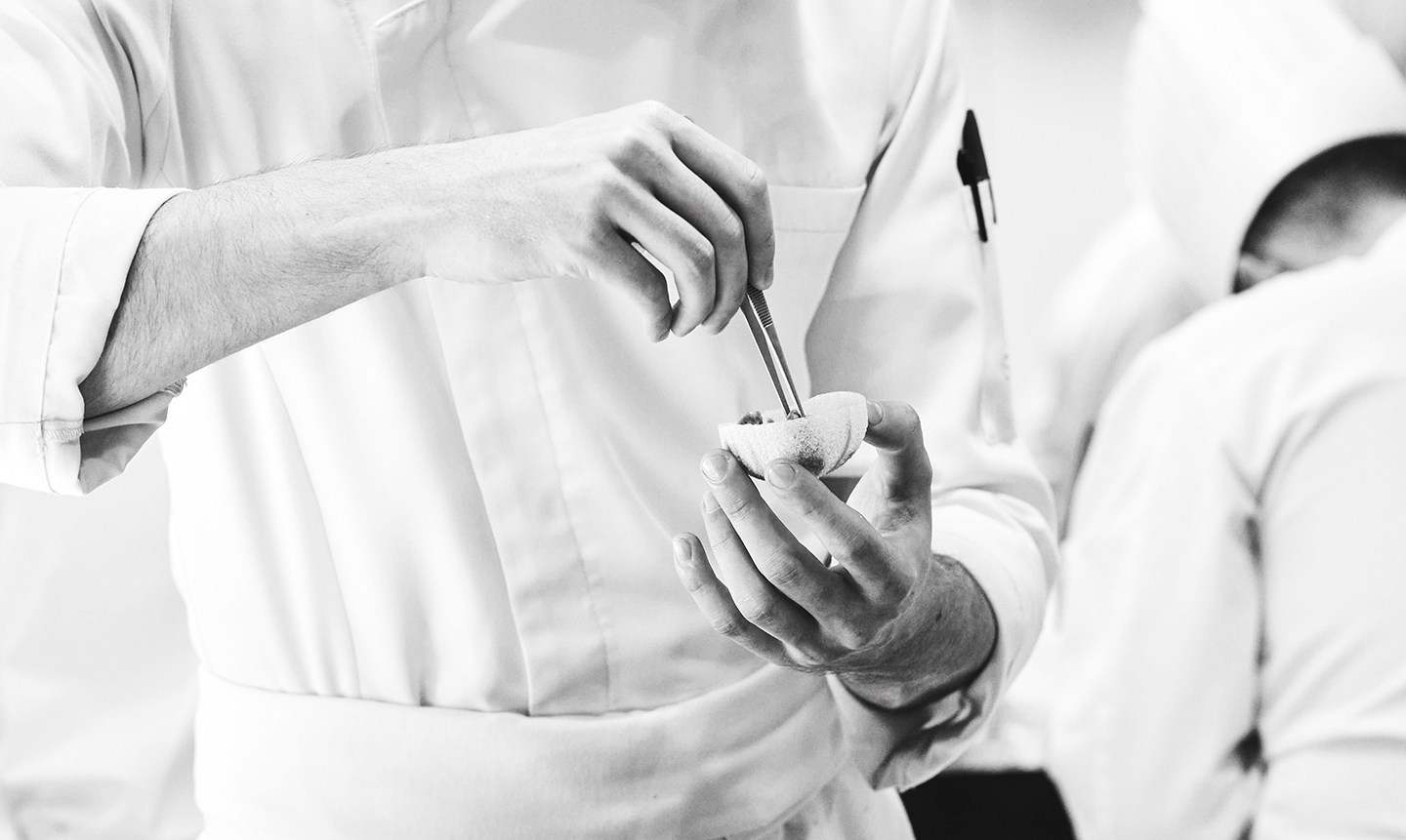Commis de cuisine préparant un plat avec précision en cuisine professionnelle.