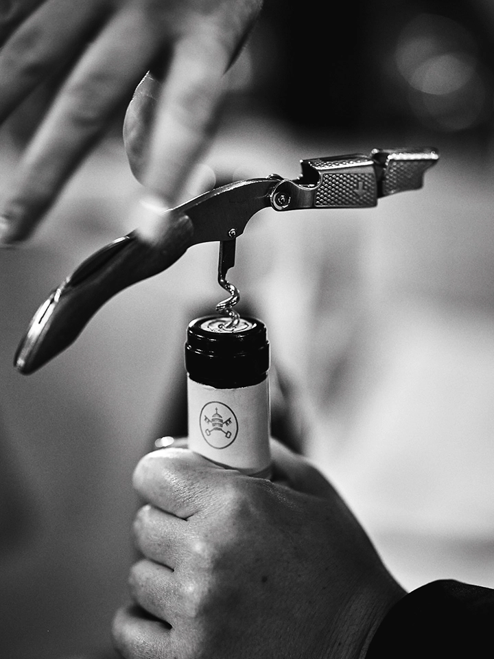 Commis sommelier ouvrant une bouteille de vin avec un tire-bouchon.