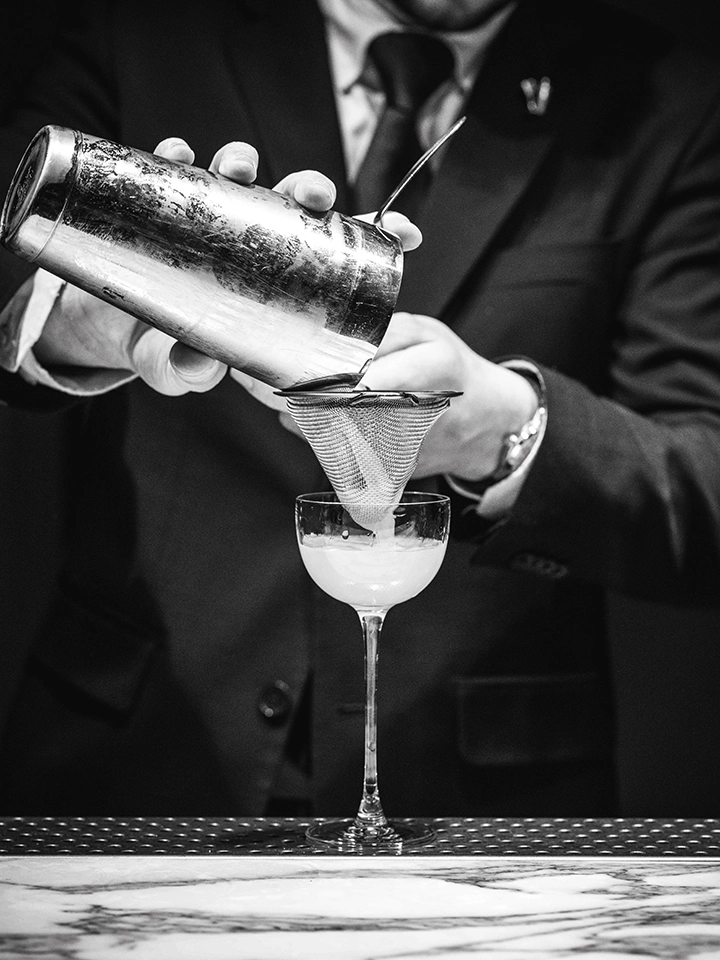Bartender versant un cocktail filtré dans un verre à pied au bar.