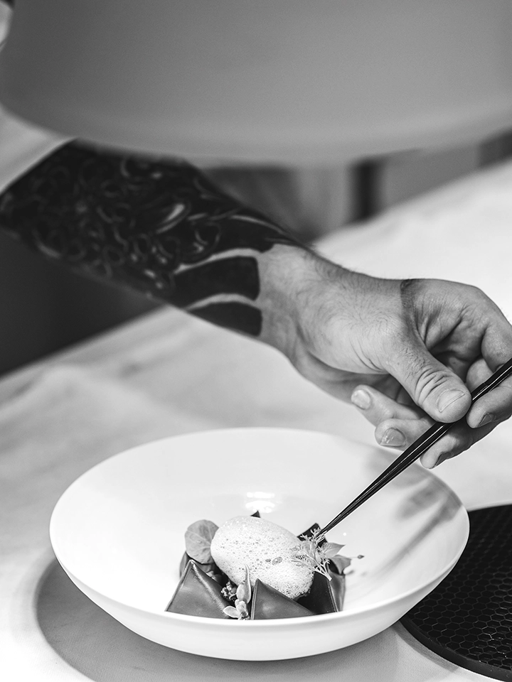 Chef de partie dressant un plat gastronomique à l’aide de pinces en cuisine.