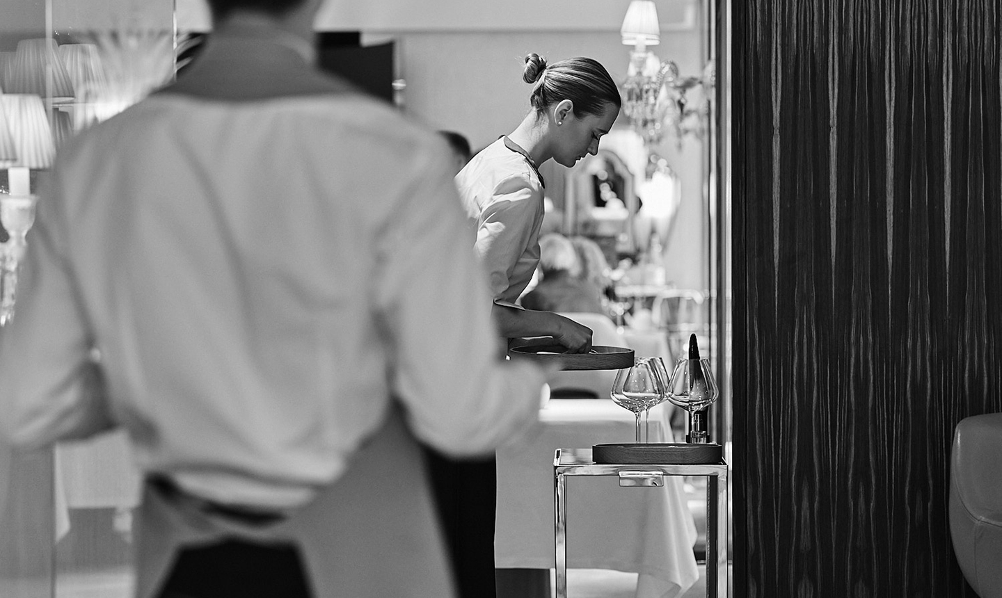 Demi-chef de rang disposant des verres à vin sur un chariot en salle.