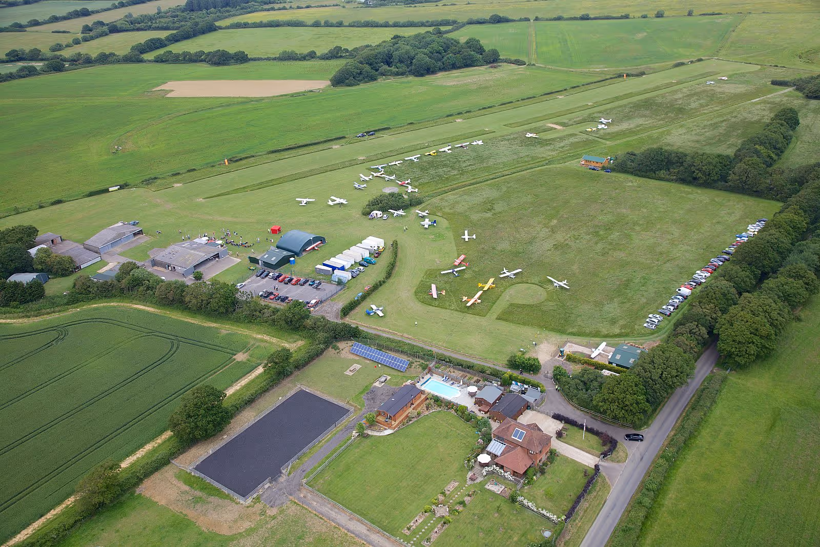 Small airplanes are parked on a grassy airfield surrounded by green fields.