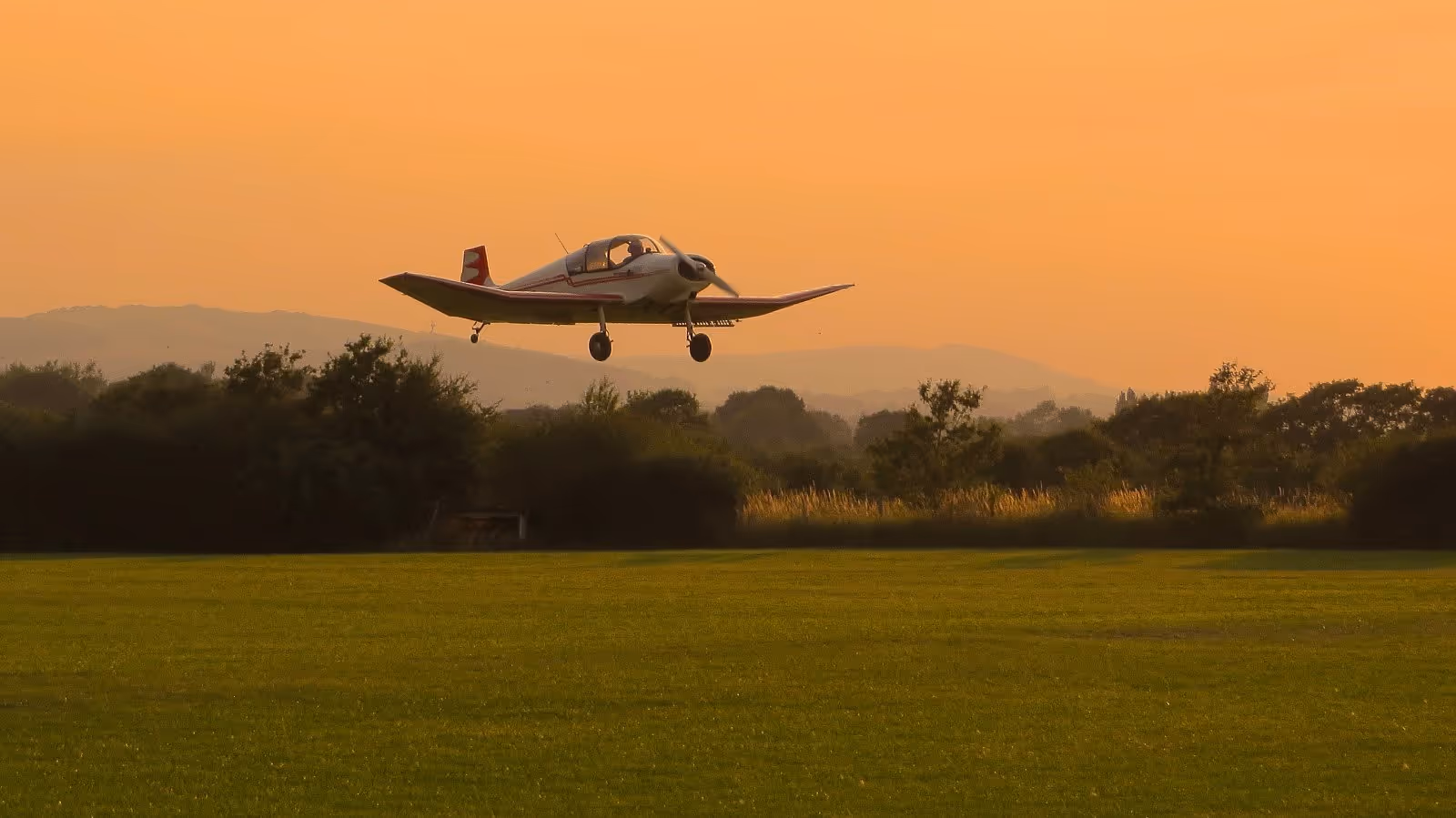 A small airplane is landing on a grassy field at sunset.