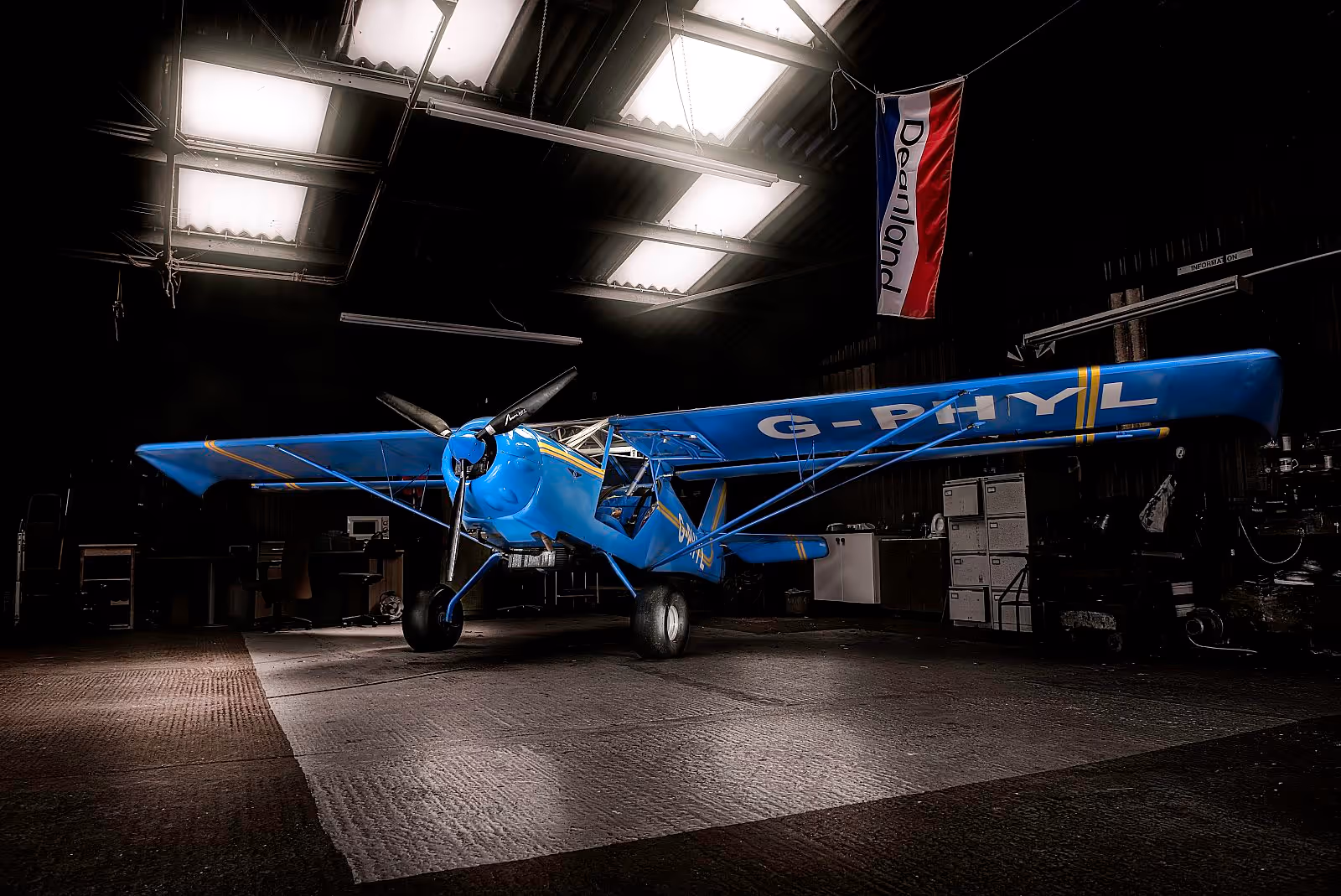 A blue vintage airplane is parked inside a dimly lit hangar.