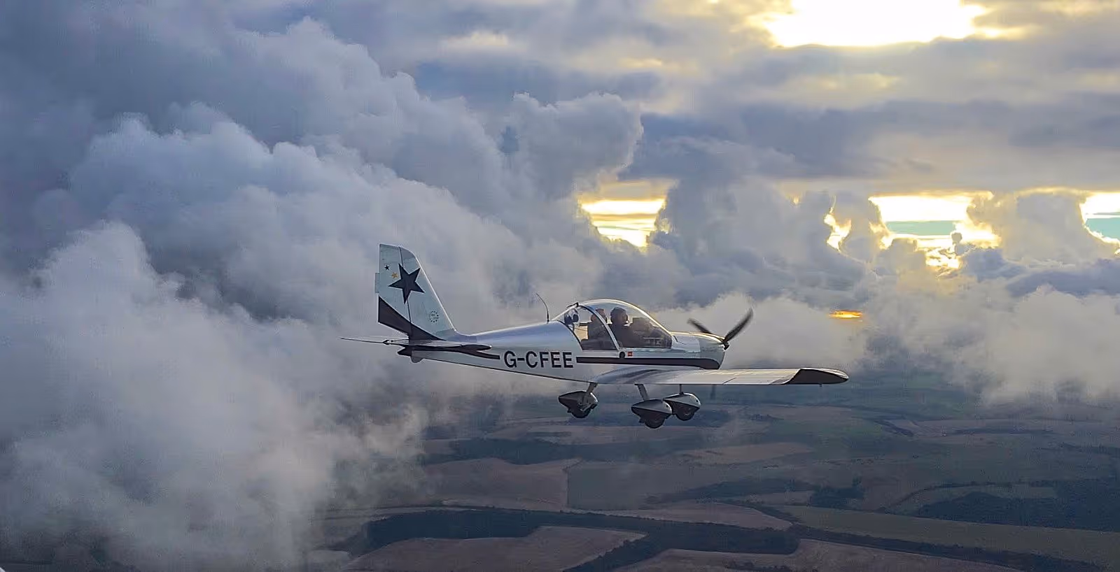 Small airplane flying through clouds with a sunset in the background.