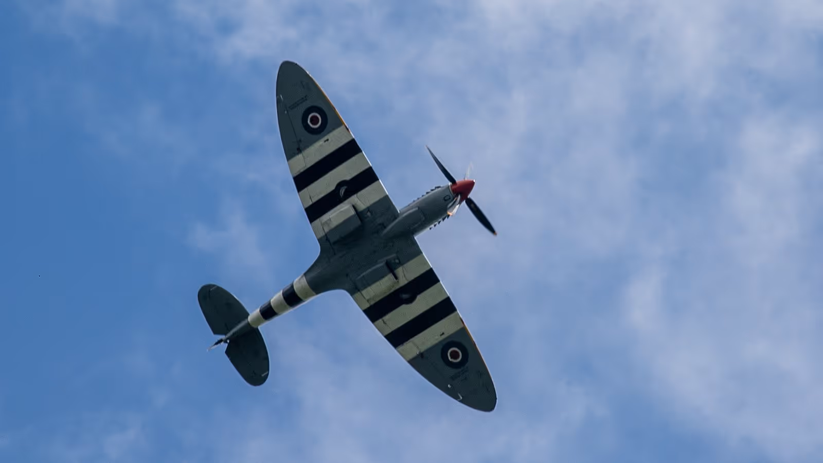 A vintage fighter plane flies overhead against a blue sky.