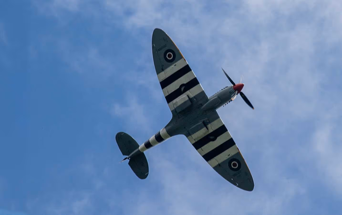 An airplane with striped wings flies in a clear blue sky.
