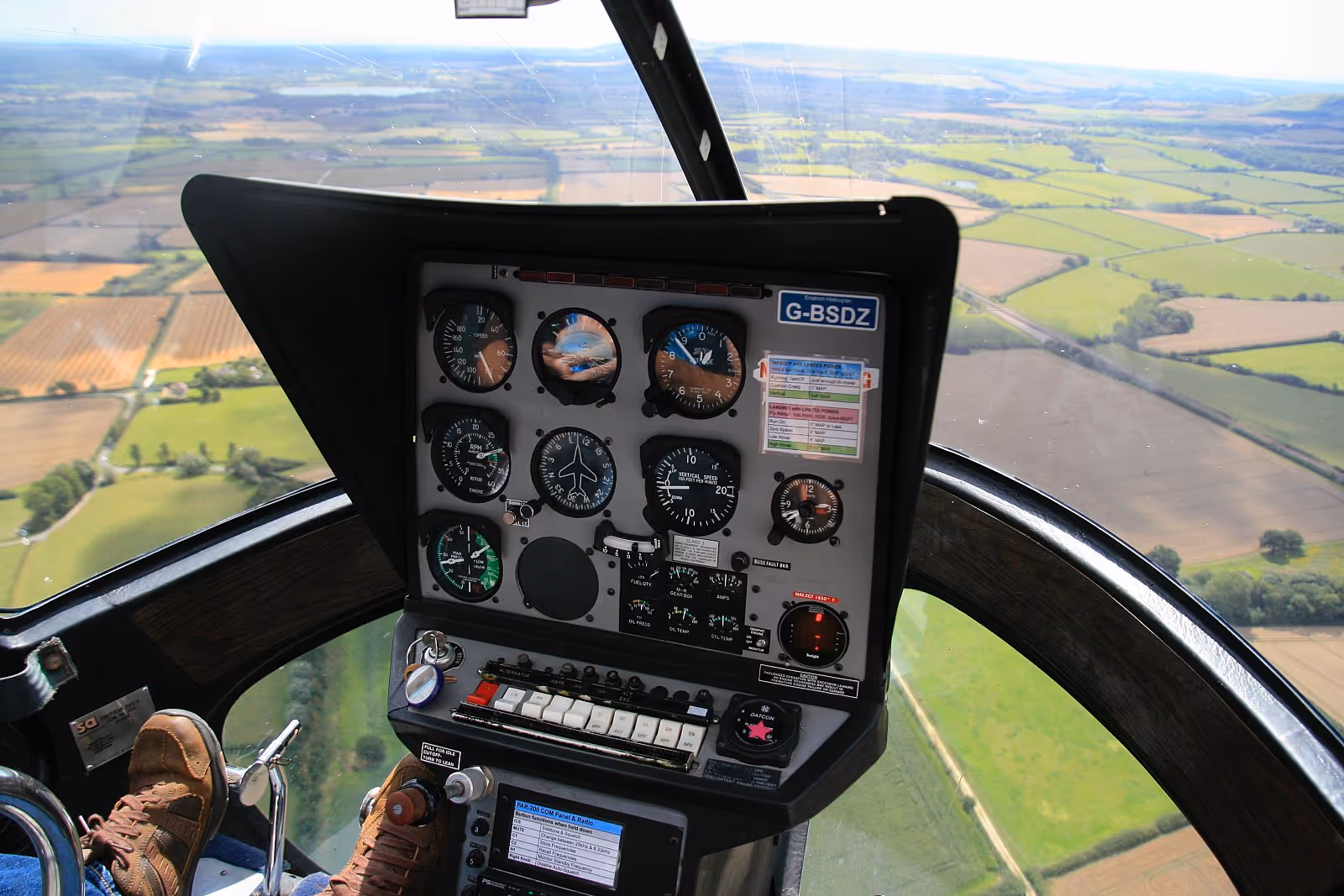 View from inside a helicopter cockpit, showing flight instruments, with fields visible through the window.