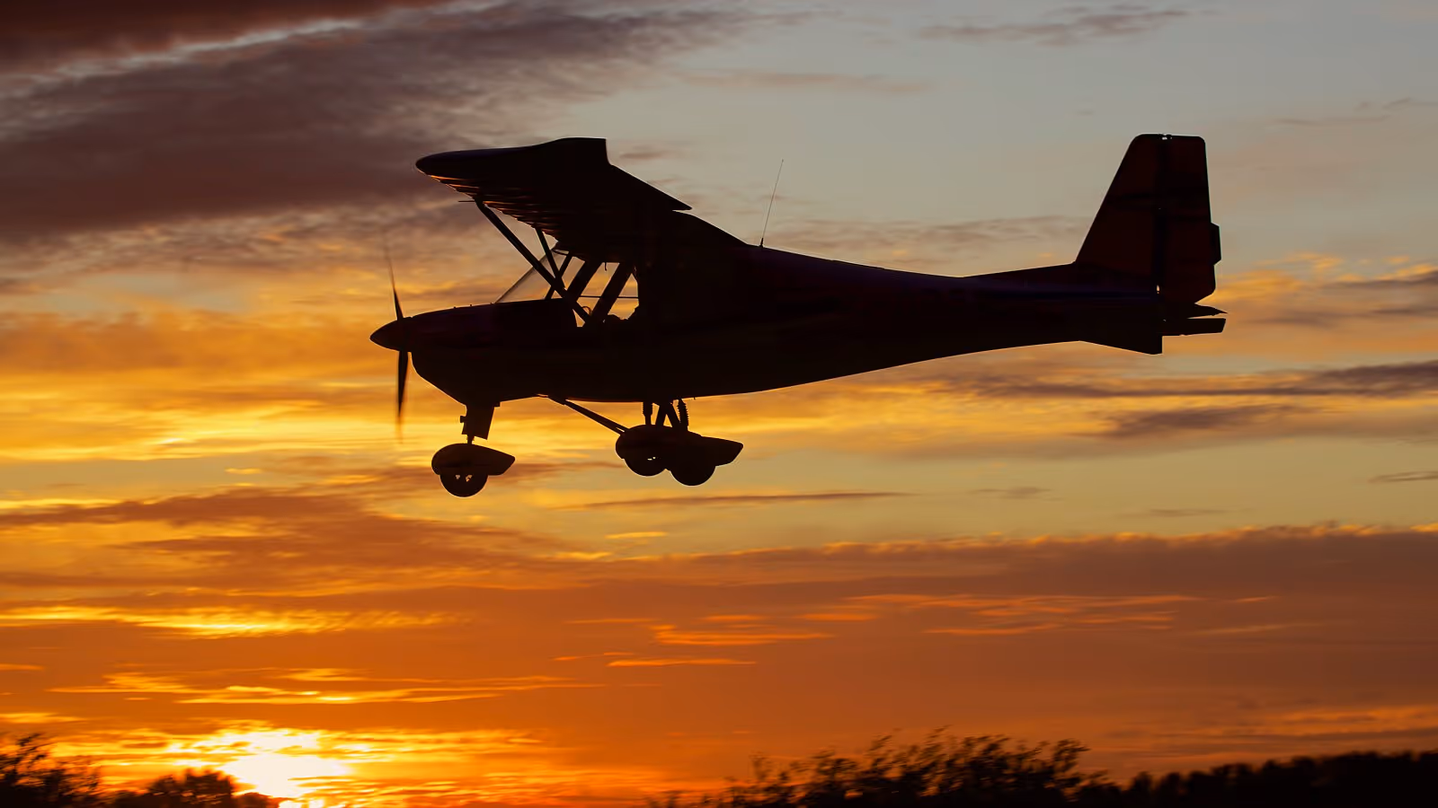 Small airplane flying during a sunset with an orange and yellow sky in the background.