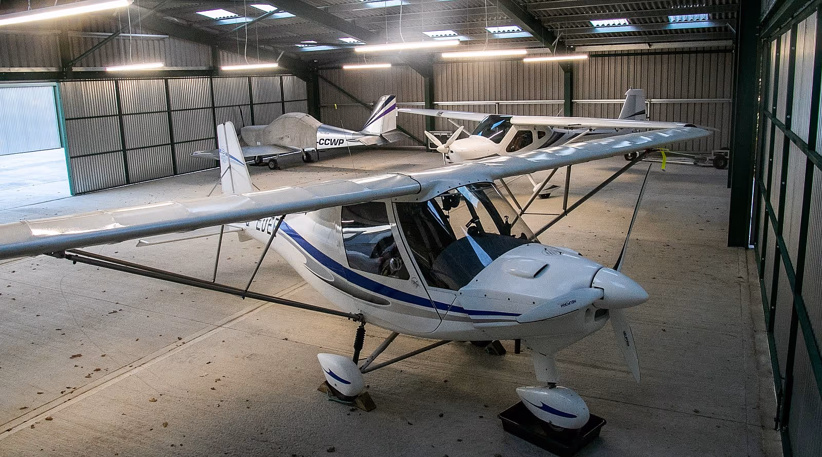 Several small single-engine airplanes are parked inside a large, well-lit hangar.
