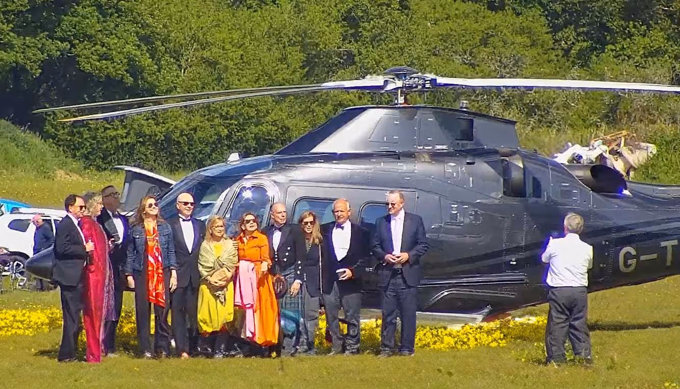 A group of people stands in front of a helicopter on a grassy field.