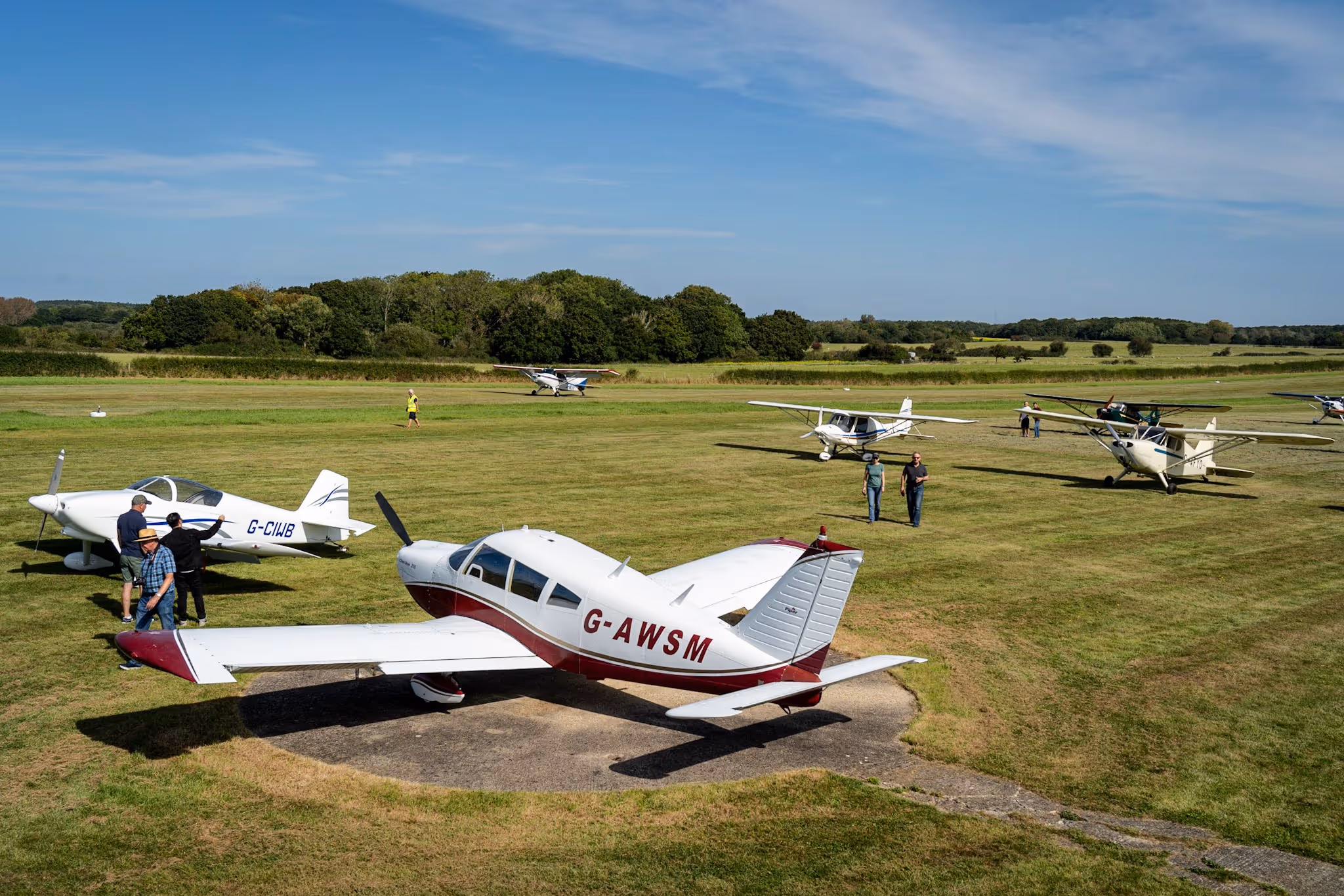 Several small airplanes parked on a grassy field with people walking around them.
