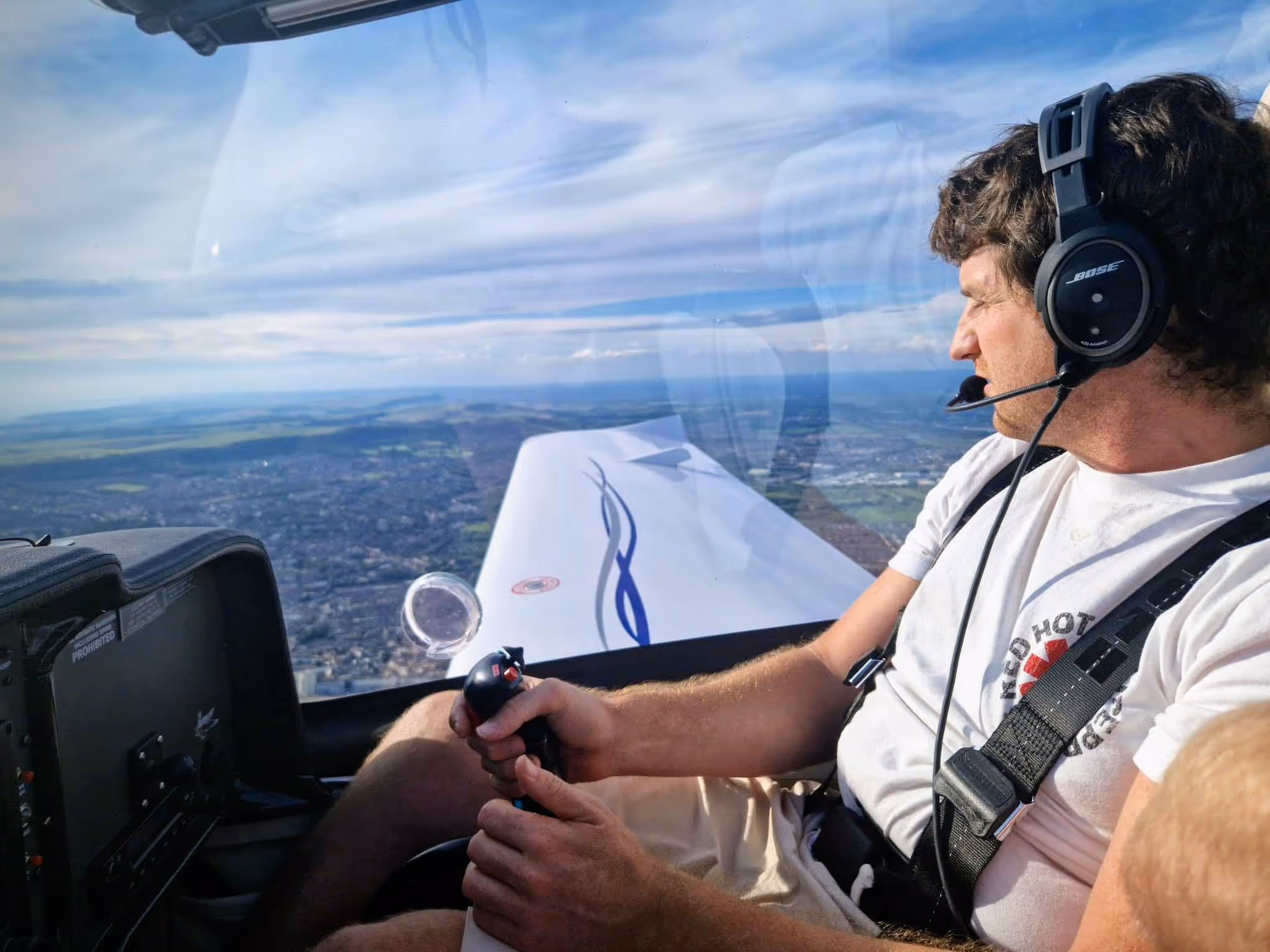 A man wearing a headset pilots a plane, looking out the window at the landscape below.