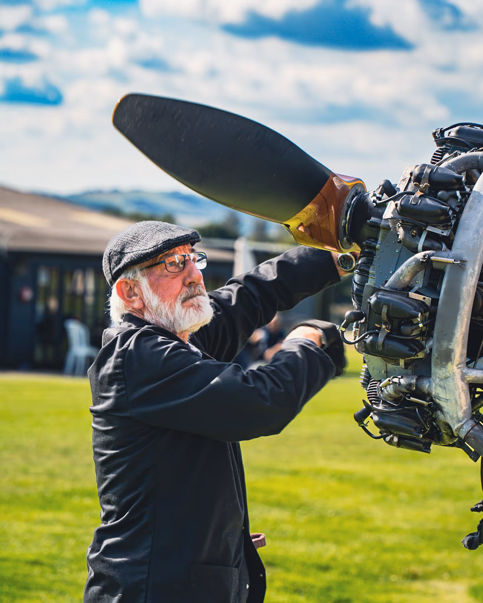 An older man with a beard inspects an airplane propeller outdoors.