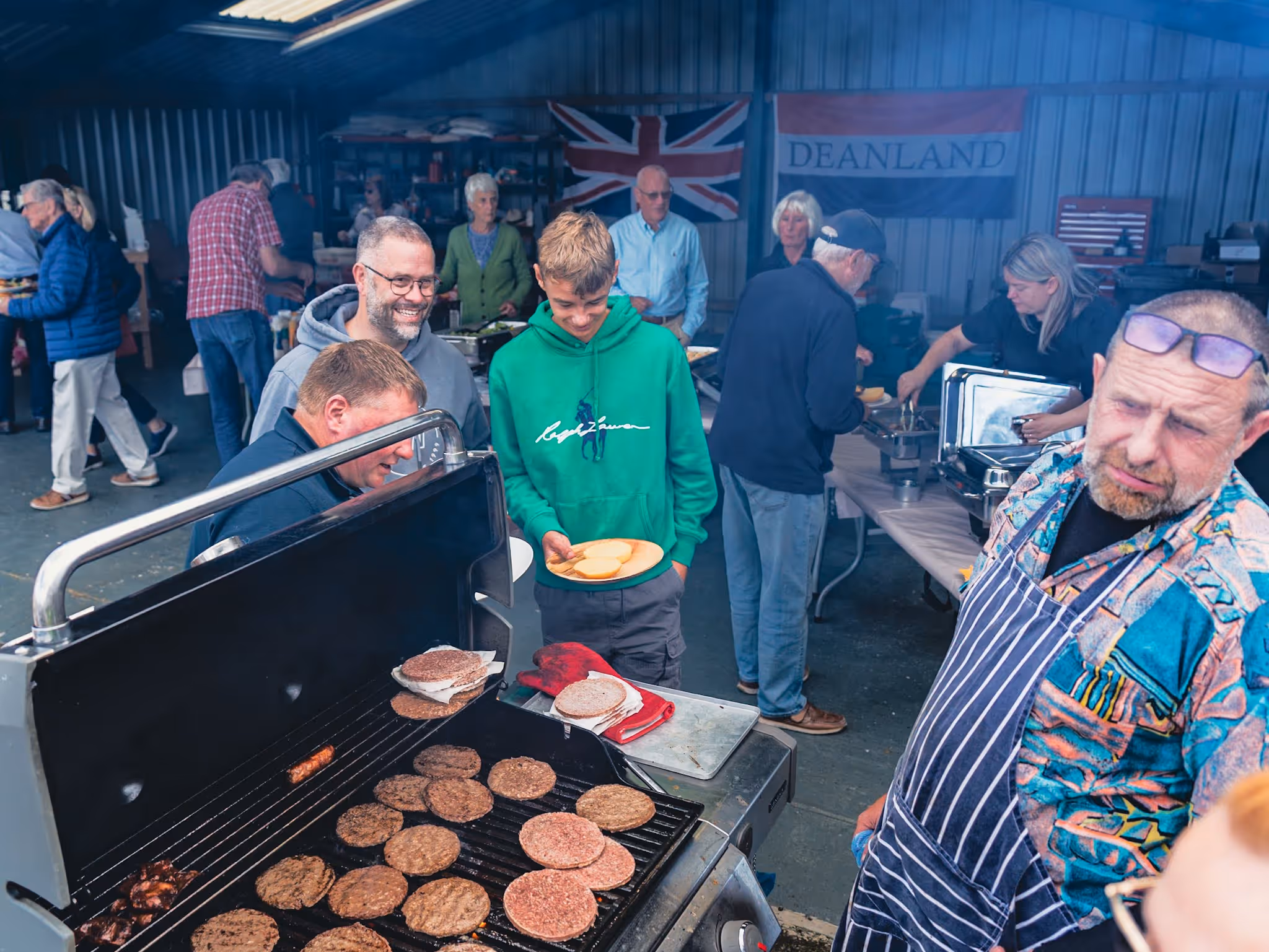 People gather around a grill cooking burgers at an indoor barbecue event.