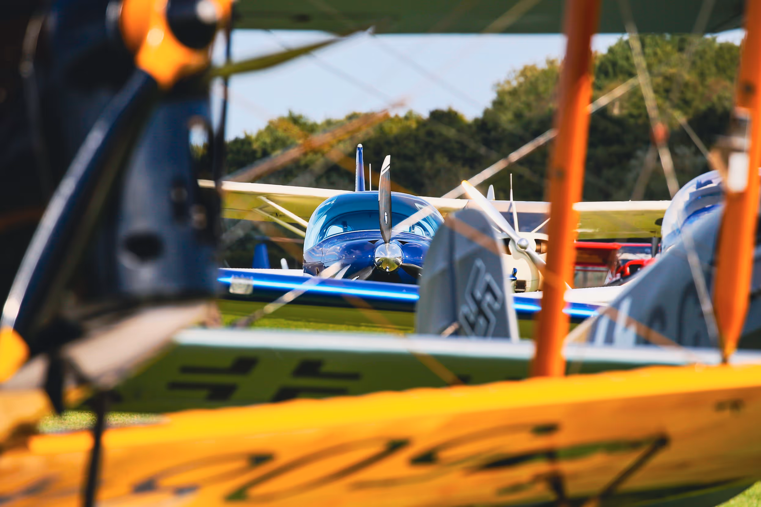Several colorful small airplanes parked closely together on a grassy field at an airshow.