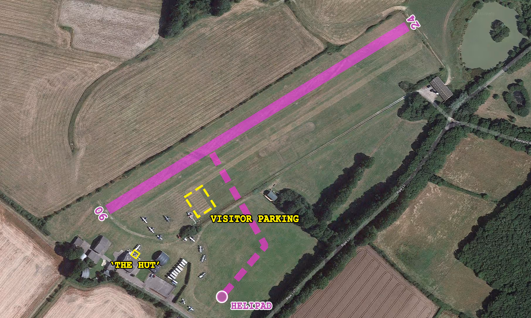 Aerial view of a field with marked visitor parking, helipad, and airplanes near "The Hut."