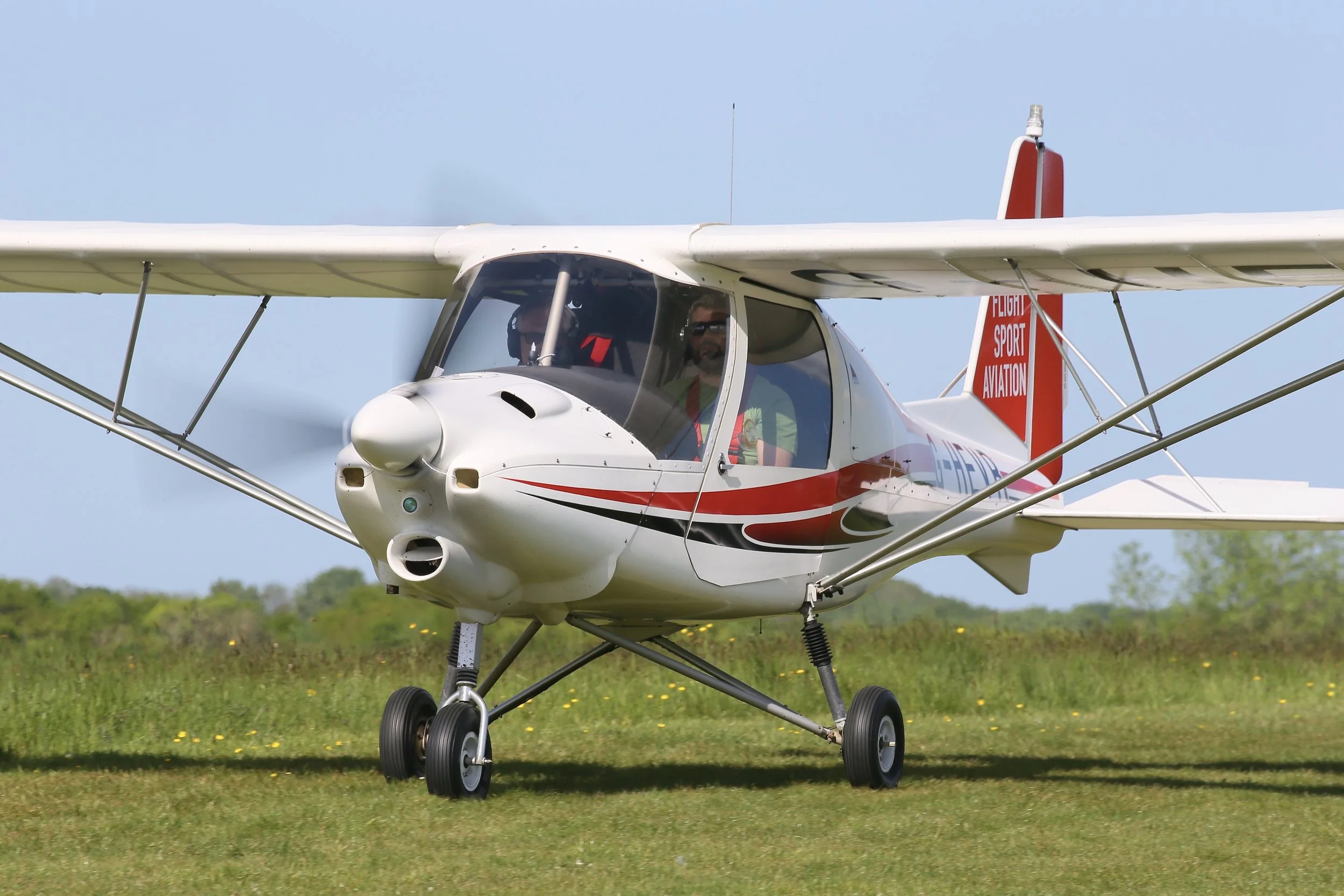 Small airplane taxiing on grass with a pilot visible in the cockpit.