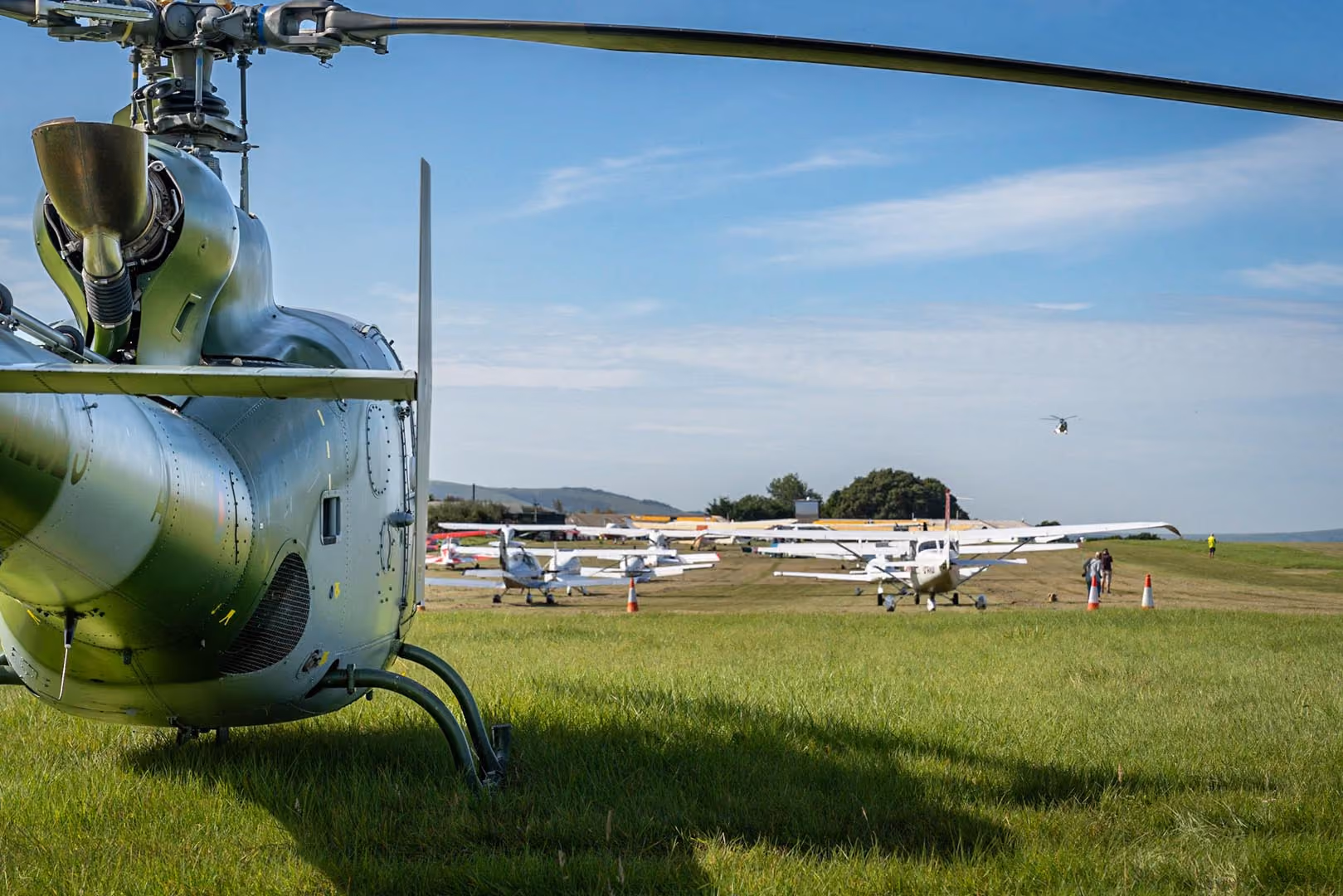 A helicopter and several small airplanes are parked on a grassy field under a clear sky.