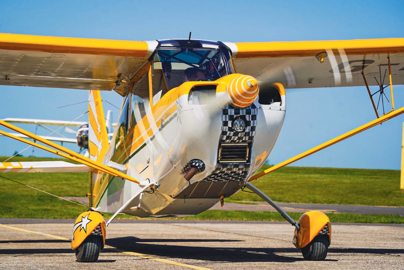 A small yellow and white propeller plane parked on a runway under a clear blue sky.