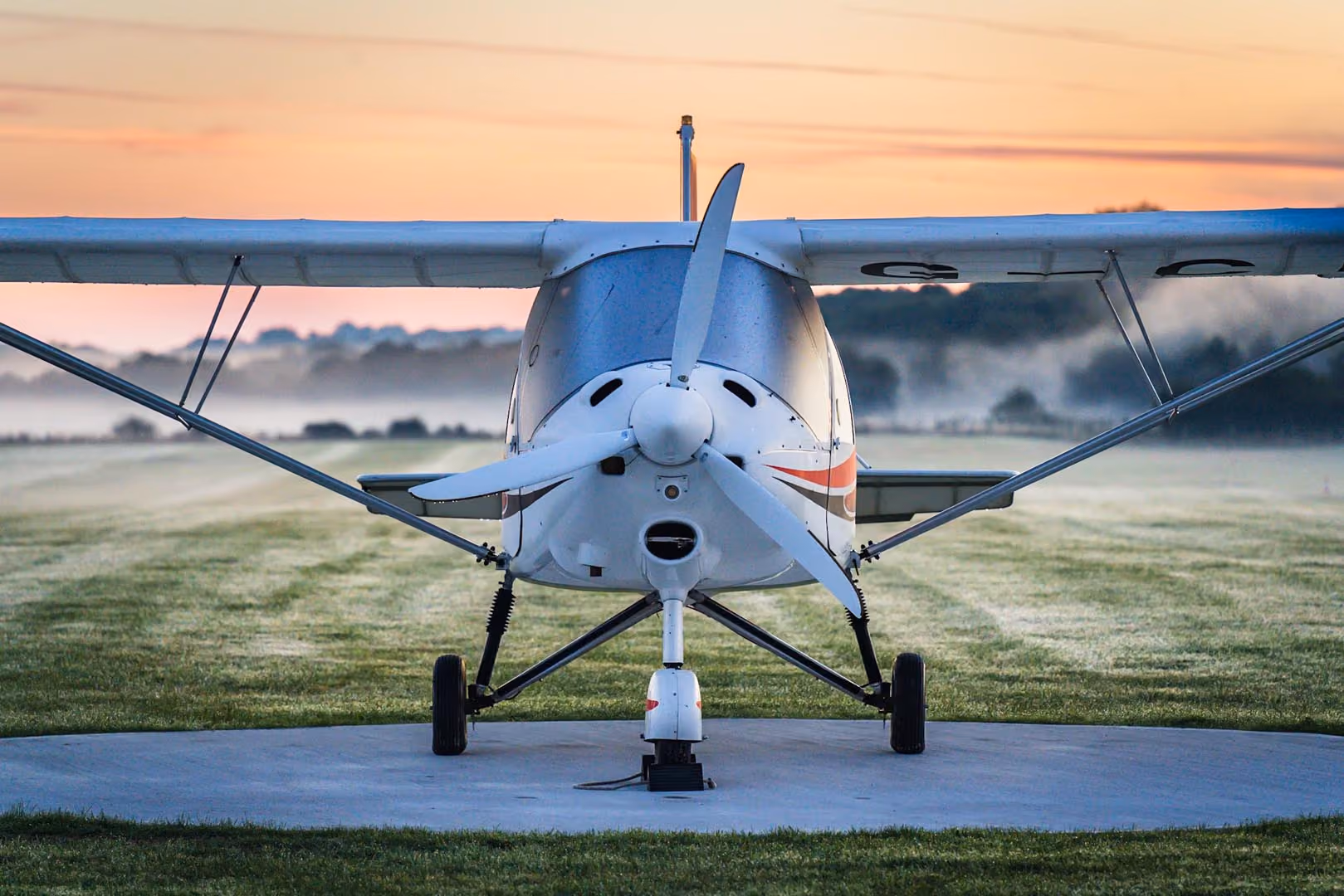 Small propeller plane parked on grassy runway at sunrise.