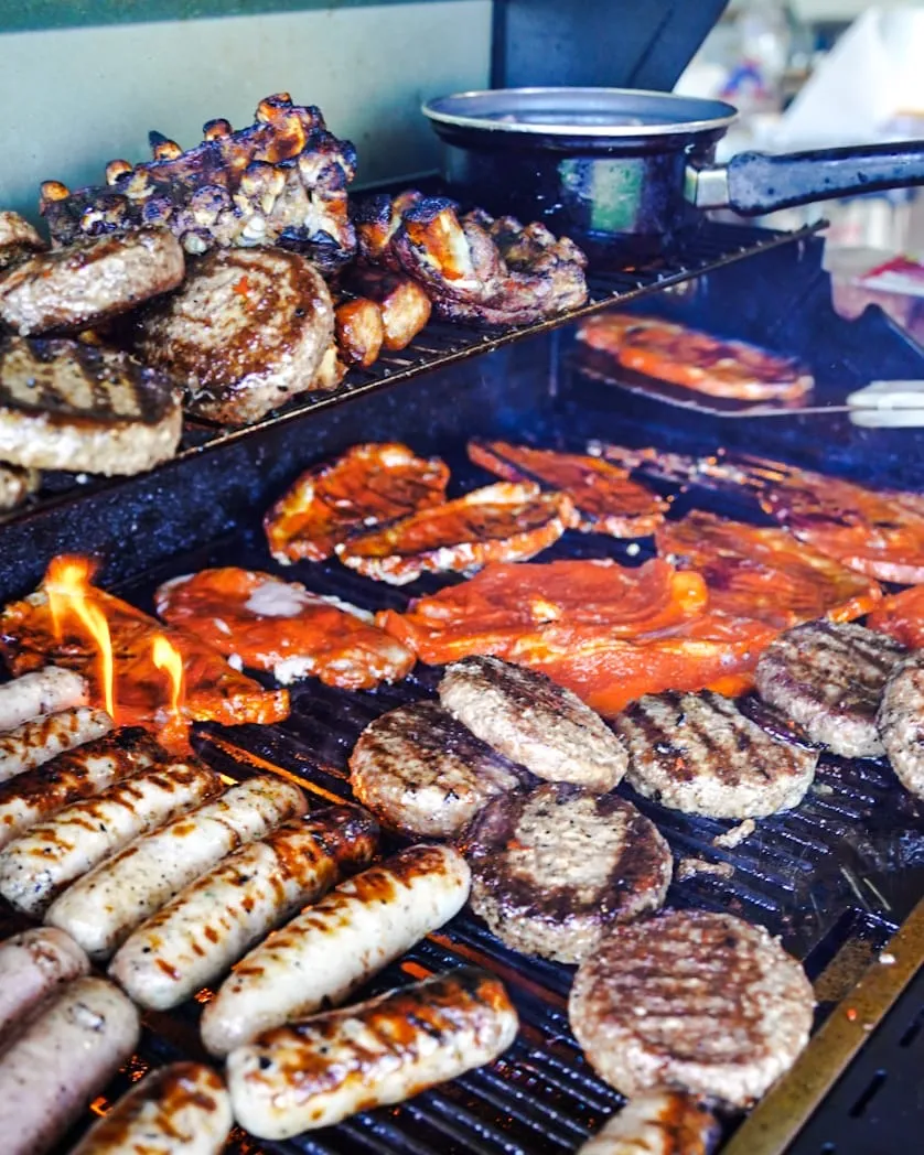 Grill with sausages, burgers, and ribs cooking over an open flame.