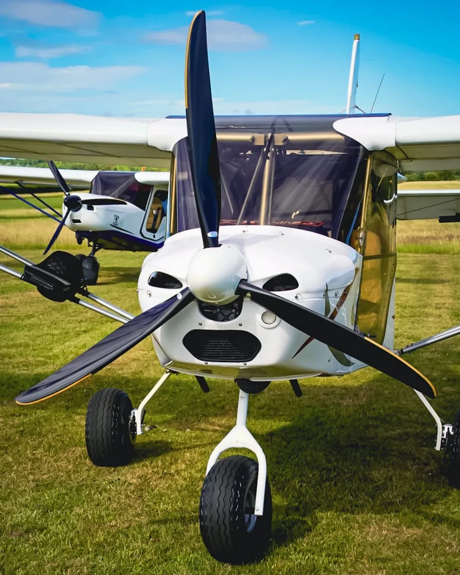 Small white airplane with a black propeller, parked on grass under a clear blue sky.