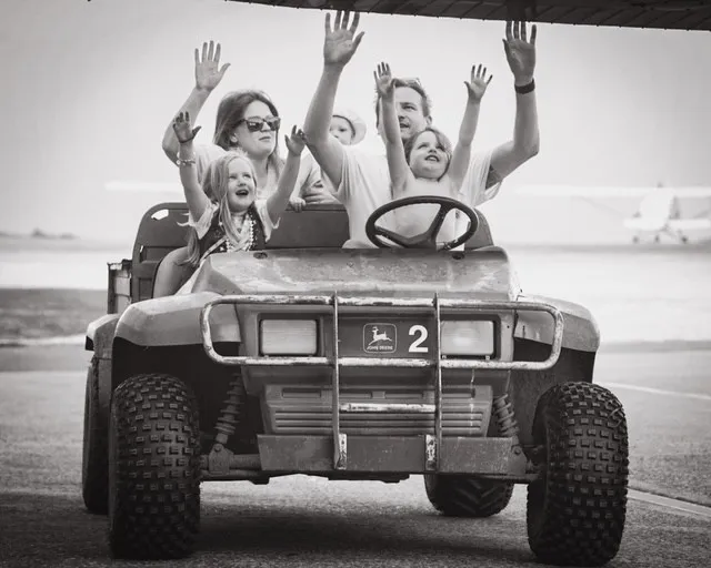A family rides in an open vehicle, smiling and waving hands in the air.